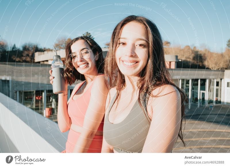 Two woman friends sitting outdoors resting after workout exercise dressed in sport clothes. Training losing weight with friends together smiling to camera happy. African arab people doing exercise.