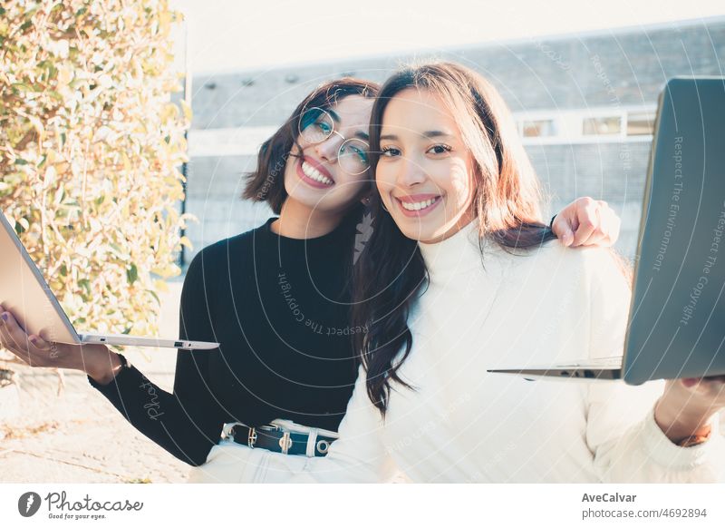 Two woman students smiling to camera and embracing while holding up laptops at the university college. Last time rush hour concept.Learning with friends new at the campus.Fraternity sorority concept