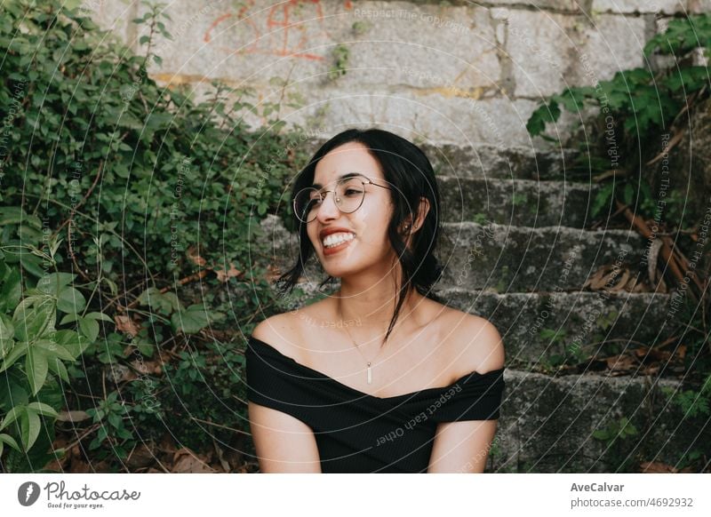 Close up portrait of a modern young woman sitting on stairs smiling away from camera. Mental health and happiness concept. Free time on young people and leisure time. Travel on vacation