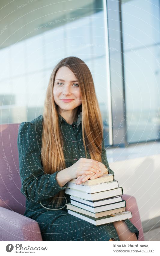 Young beautiful woman in green dress holding a stack of books. Female student holding books to study. Education and knowledge. Millennial lifestyle. University library or bookstore. Bookworm.