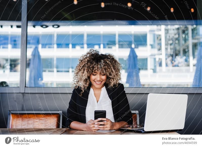 beautiful hispanic afro business woman in cafe working on laptop and mobile phone.Business and tech computer networking drinking coffee terrace outdoors goggles