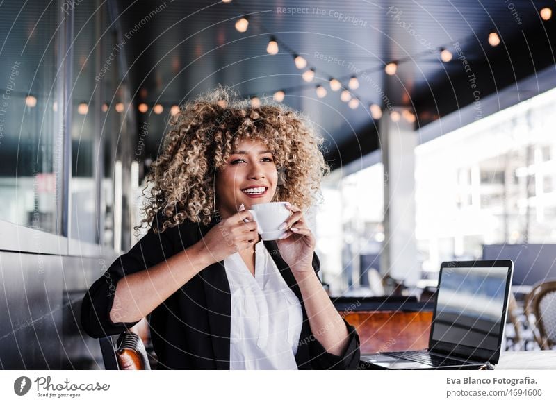 beautiful hispanic afro business woman in cafe working on laptop and mobile phone.Business and tech computer networking drinking coffee terrace outdoors goggles