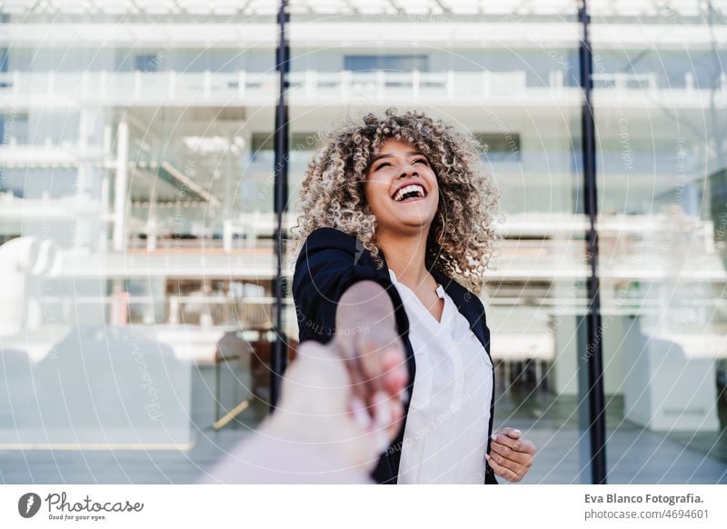 beautiful laughing business woman in city holding hand with friend. Buildings background happy friends afro hispanic mobile phone skyscraper building young