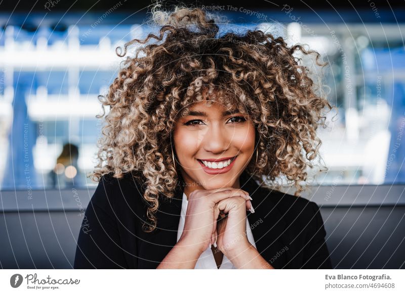 portrait of smiling confident business woman in cafe. Business concept afro hispanic terrace happy mobile phone city skyscraper building young curly hair