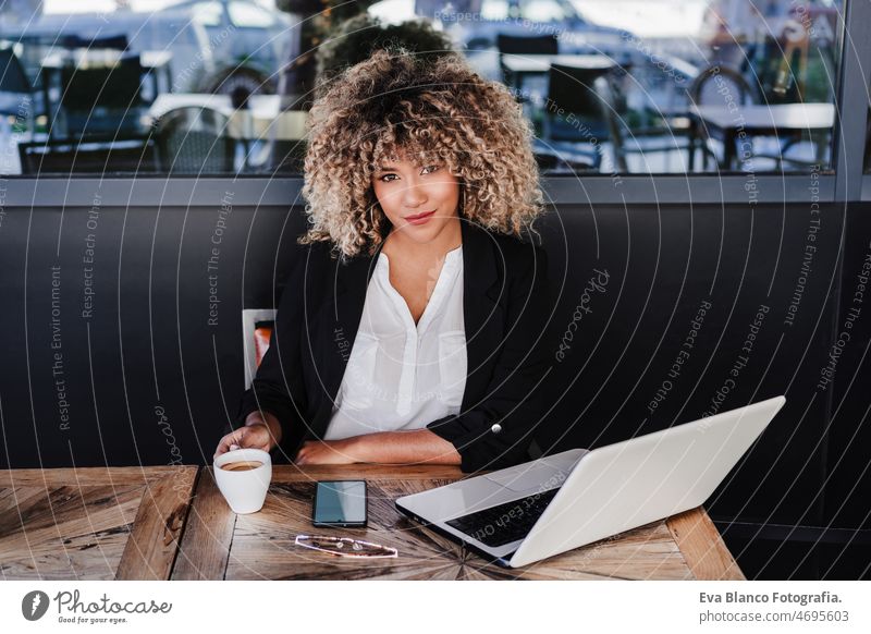 confident hispanic afro business woman in cafe working on laptop and mobile phone.business,lifestyle computer networking drinking coffee terrace outdoors