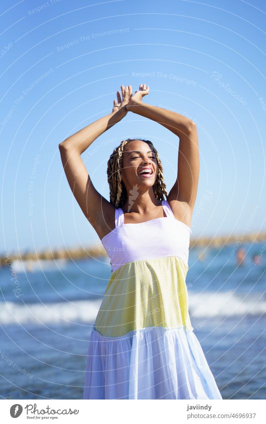 Black woman walking along the shore of the beach wearing a beautiful long dress. girl model female zizi afrobraid braids fashion fashionable young person summer