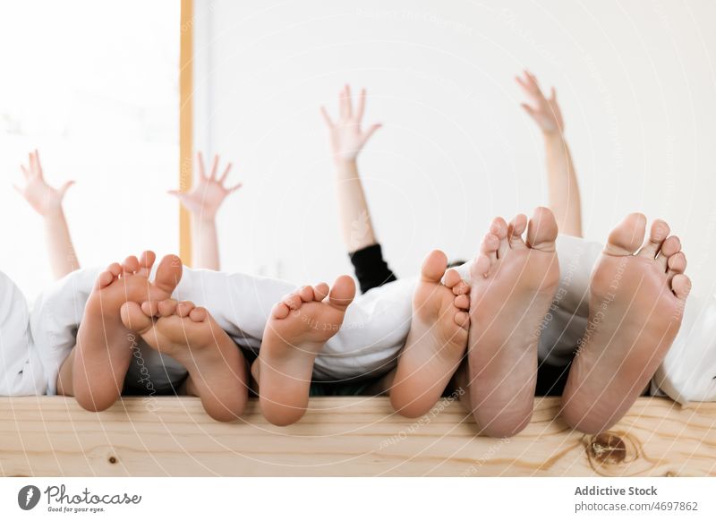 Unrecognizable siblings lying barefoot in bed little children care family kids healthy room raised arms comfort brother childhood finger sister human female