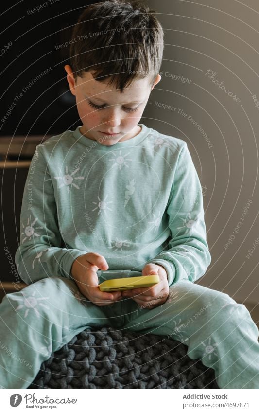 Boy in pajama playing on smartphone boy kid childhood videogame pastime morning domestic room apartment adorable barefoot flat cute home residential nightwear