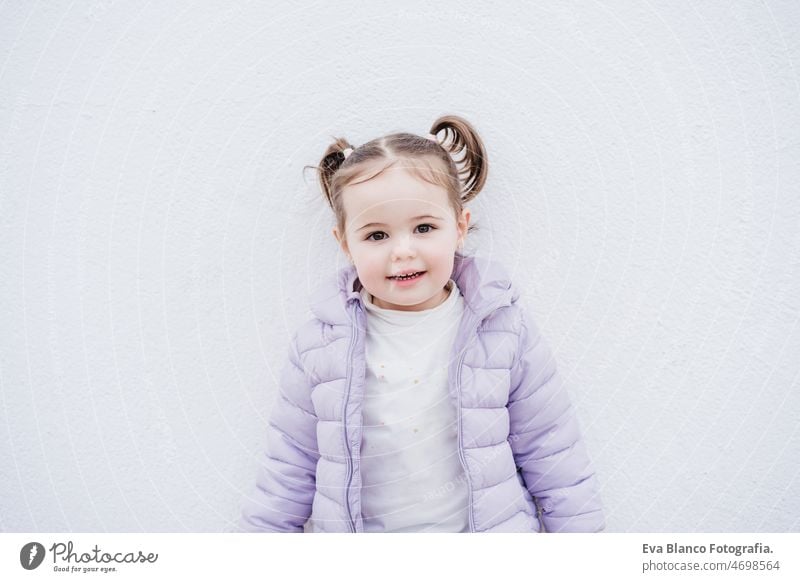 portrait of beautiful caucasian two year old baby girl smiling over white background. childhood outdoors city coat cold winter happy pony tail little small