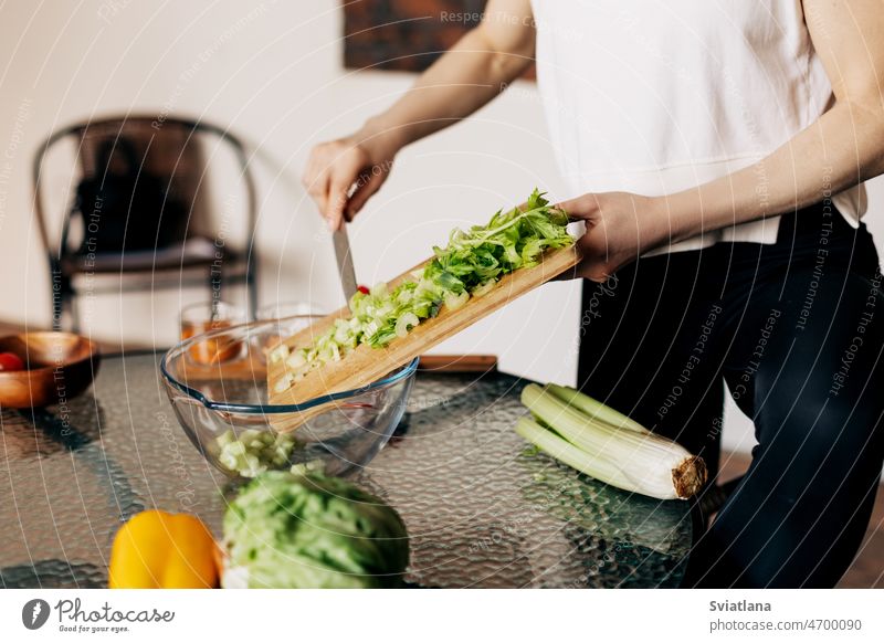 A woman cuts celery on a wooden board and transfers it to a transparent salad plate fresh stalk sliced cutting freshness vegan health healthy green natural food