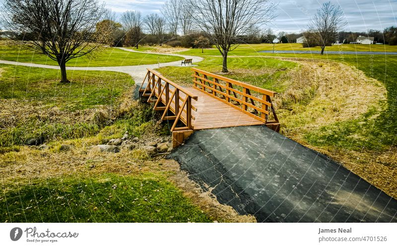 Rural scene at a park with old bridge over dried up stream in autumn outdoors rural fall season footbridge footpath trail tree branches grass river drought dry