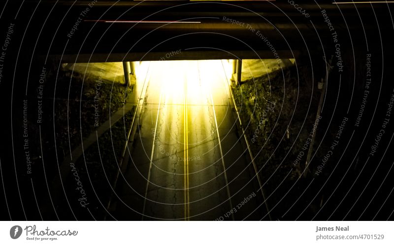 A bright underpass of a highway bridge at night. A thin line of motion from a car can be seen on top of the bridge. outdoor outdoors outside nobody empty