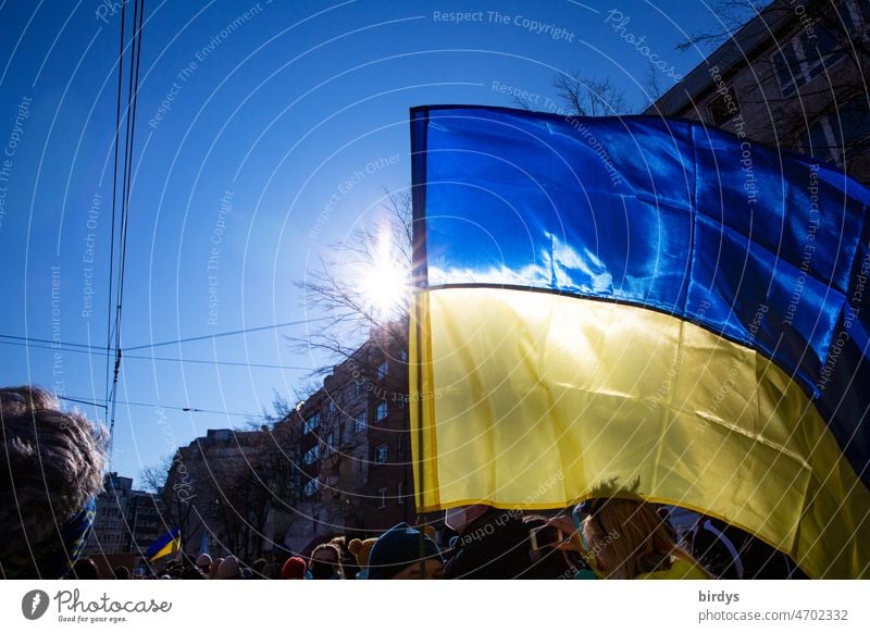 waving Ukrainian flag at peace demonstration with bright sun in backlight. City Ukraine Peace demonstration Ensign blowing Radiant sun demonstrators Ukraine war