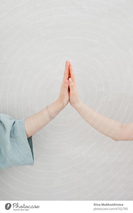 Hands together palm to palm as gesture and symbol of unity and friendship with neutral grey wall as background. Feminism. Women supporting women. Female support, friendship and unity. Strong together.