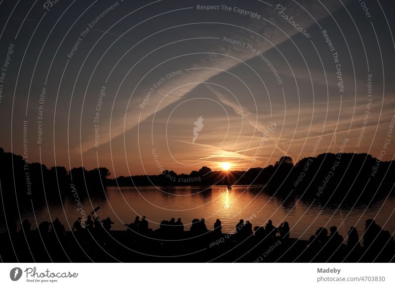 Students in the evening in the summer at the sunset over the Aasee in Münster in Westphalia in the Münsterland region of Germany Dark reflectiveness