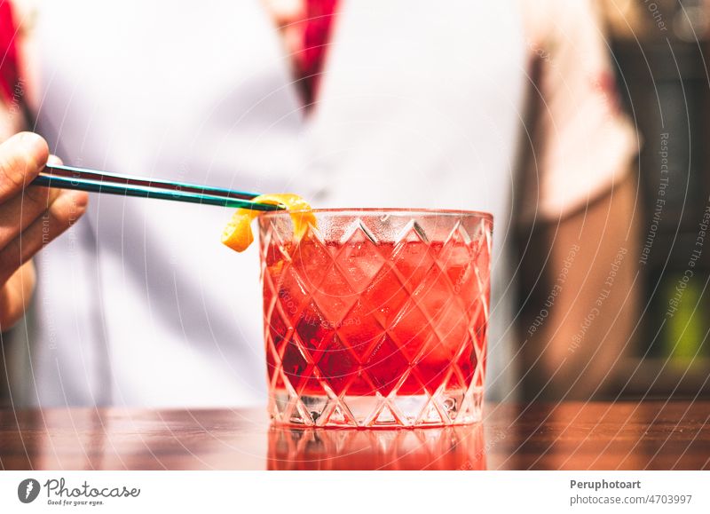 Close up shot of bartender hands preparing negroni cocktail with grapefruit. He is putting some essence from grapefruit skin into the cocktail glass on counter.