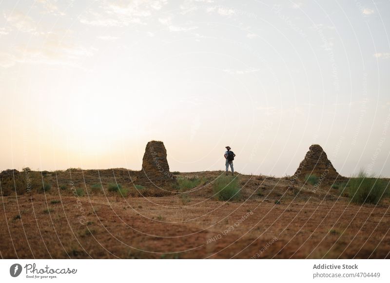 Anonymous traveler standing in desert field trip adventure arid journey explore barren drought vacation dry bush vegetation hat vegetate waterless tourism