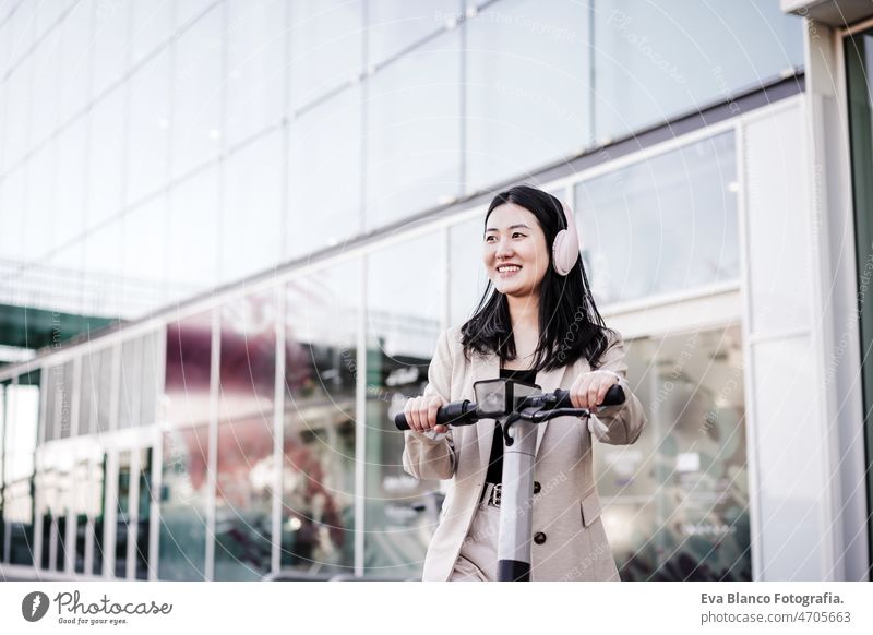 chinese business woman renting electric scooter in city,wearing headphones.sustainable transport music urban modern sustainability public transport asian young