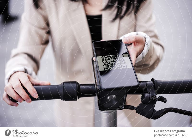 Businesswoman unlocking electric push scooter through smart phone on road. sustainable transport qr code unblocking unrecognizable touch wireless renting asian