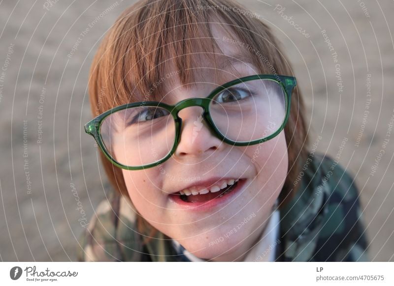 child wearing glasses looking curious at the camera and smiling Emotions Mysterious Identity Uniqueness Smiling face smilingly laughing child fortunate joyfully