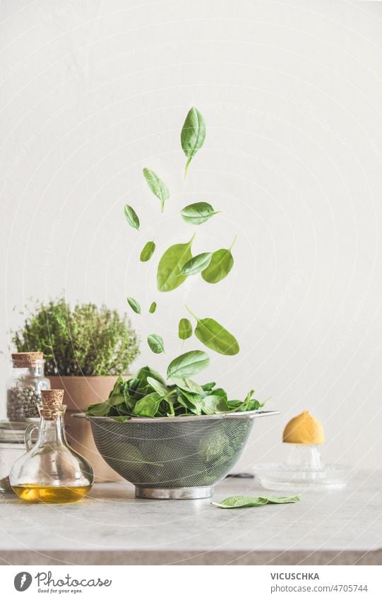 Falling green spinach leaves in sieve on kitchen table with ingredients falling olive oil potted herbs lemon pepper food levitation concept healthy cooking