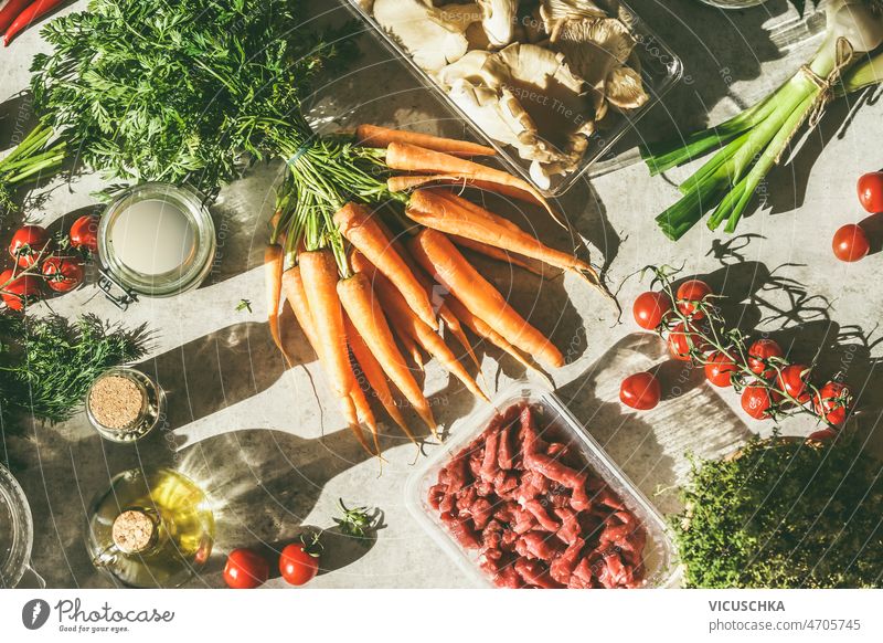 Food background with various healthy cooking ingredients on kitchen table food raw meat grey sunlight carrots tomatoes oil scallions oysters mushrooms home