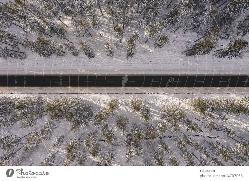 Aerial drone view of road in idyllic winter landscape at sunset. Street running through the nature from a birds eye view forest aerial snowy sunlight above