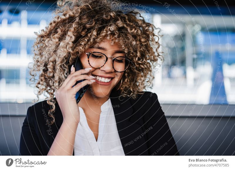 smiling hispanic afro business woman in cafe working on laptop and mobile phone. tech and lifestyle computer networking drinking coffee terrace outdoors goggles