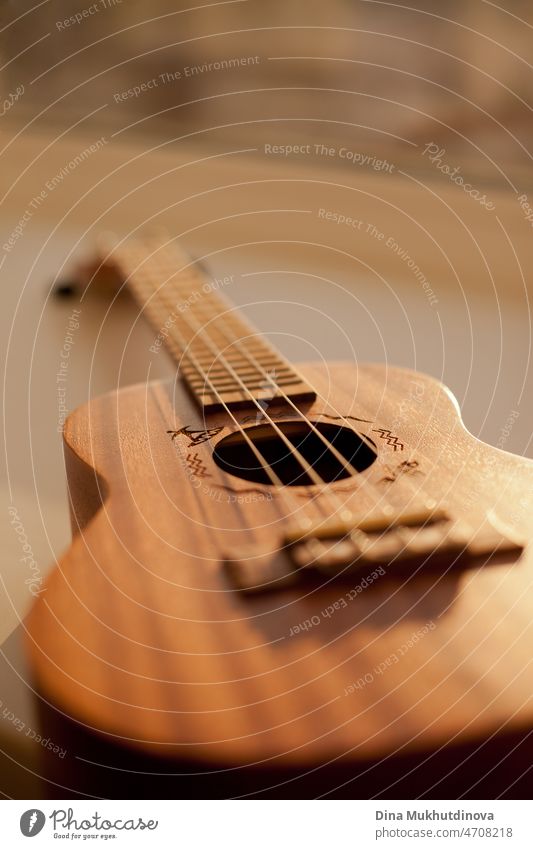 Ukulele Hawaiian small guitar music instrument at sunset closeup photo. Beige brown gold colour palette shot with ukulele lying on windowsill in soft natural light.