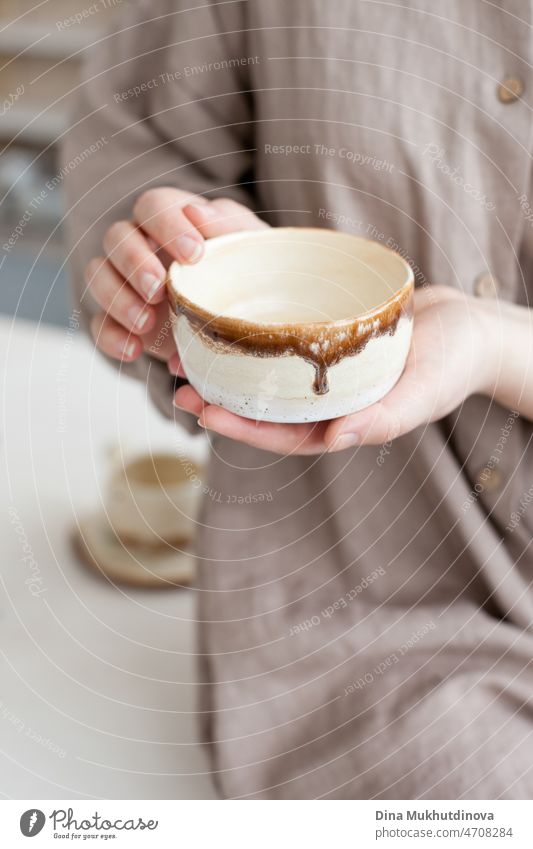 Woman holding a handmade artisanal pottery bowl in her hands. Neytral colors hobby tableware at pottery studio, creative and inspirational people creating things and products in small business.