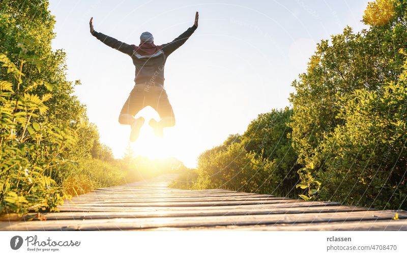 Happy young man jumping with raised hands and legs, and enjoying life over a Wooden jetty at sunset happy free nature path trampoline air girl walkway weekend