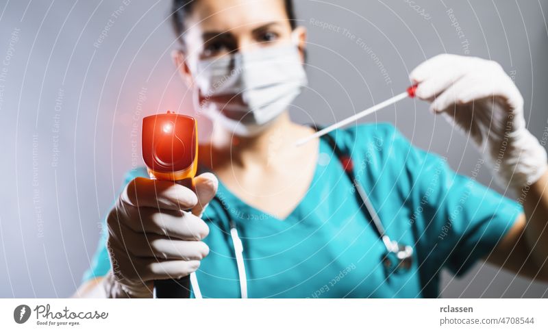 Checking the temperature with a laser thermometer by a person in a protective suit, protective mask and smear tube test. Thermometer (thermometer gun) held in hands wearing disposable gloves.