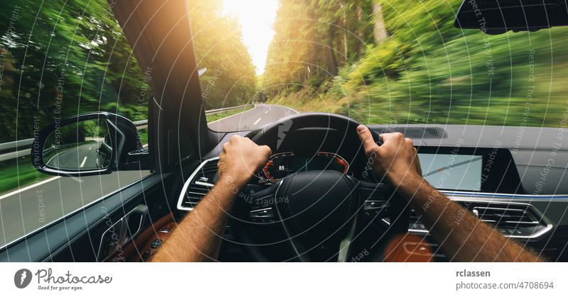 Hands of car driver on steering wheel, fast driving car at spring day on a country road, having fun driving the empty highway on tour journey - POV first person view shot