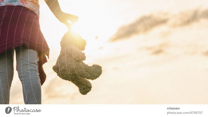 lonley girl holding a teddy bear at sunset. copyspace for your individual text. childhood lonely adult dream attractive autumn scary dramatic clouds background