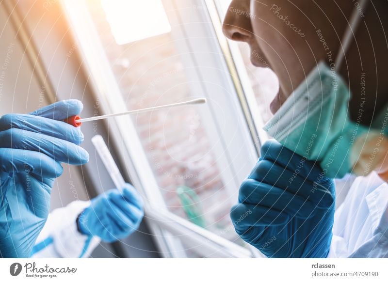 Medical in protective clothing takes COVID-19 swab test tube from mouth at Covid-19 test center during coronavirus epidemic. PCR DNA testing protocol process.