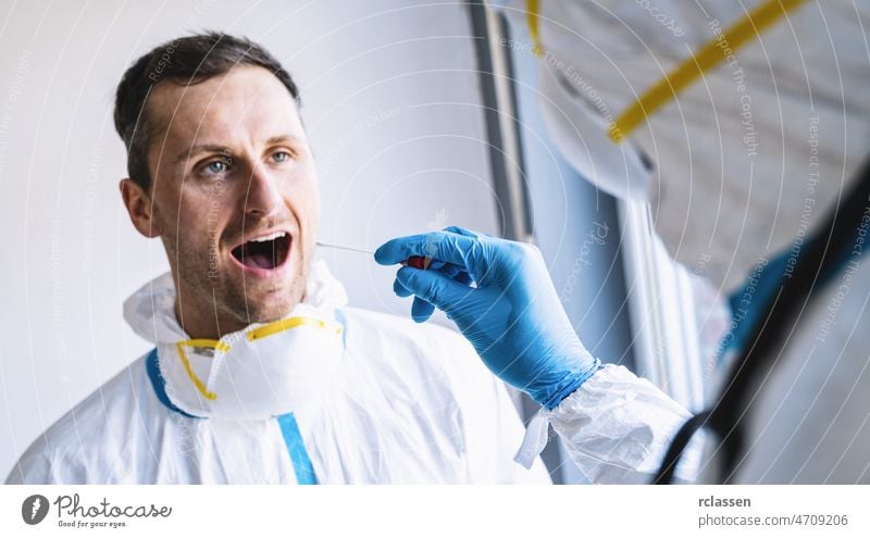 Medical professional in protective clothing takes swab test tube from mouth of a Exhausted clinician at a Covid-19 test center during coronavirus epidemic. PCR DNA testing protocol process.