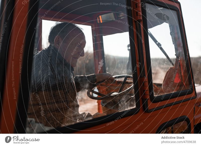 Old man driving tractor in rural field senior farmer drive cart plantation agriculture countryside male tree carry harvest work old suburb branch farmland