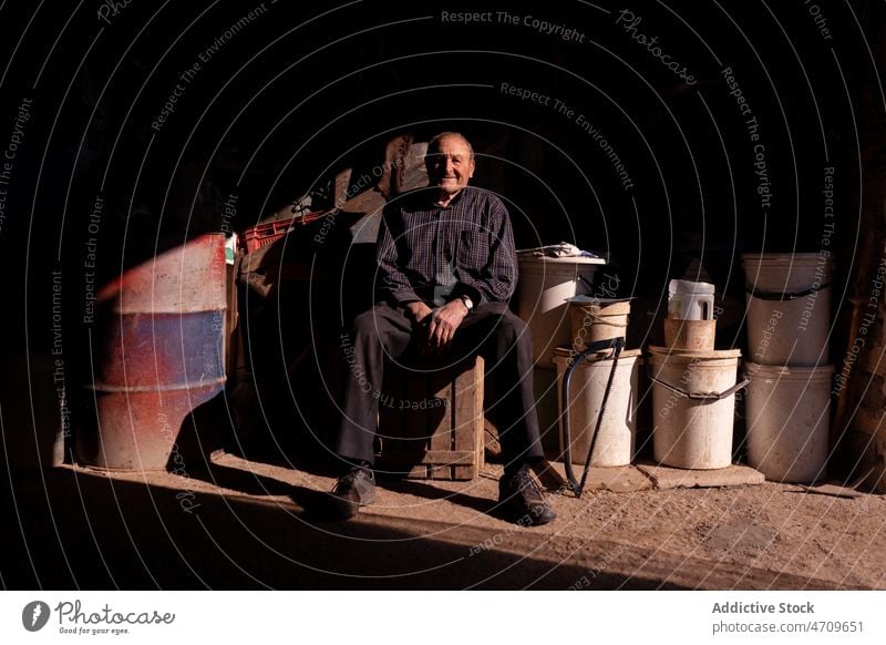 Old man sitting on wooden container in garage senior rural crate shed suburb happy countryside storage retire male box aged smile elderly pile glad farm delight