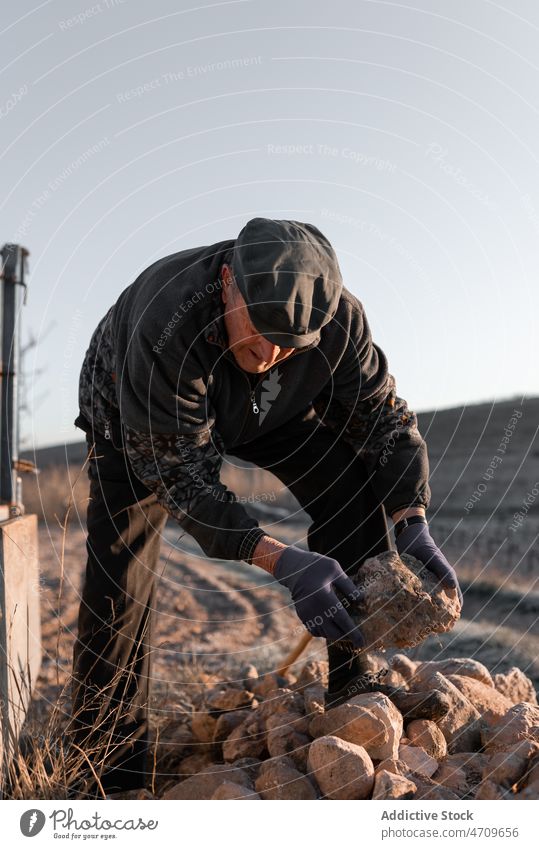 Old man with rough rock in hand senior stone boulder mineral collect old pick detail male aged stand retire elderly pensioner sunlight street sunshine wrinkle