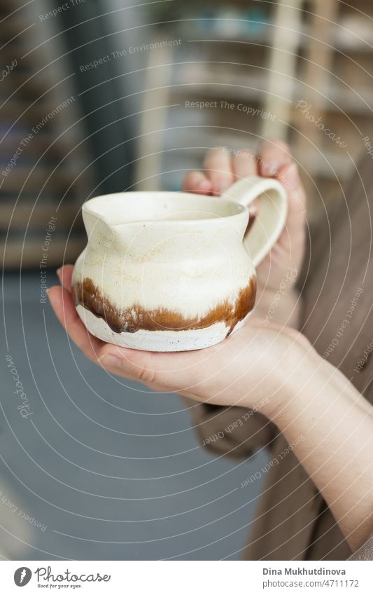 Woman holding a handmade artisanal pottery jug in her hands. Neytral colors hobby tableware at pottery studio, creative and inspirational people creating things and products in small business.