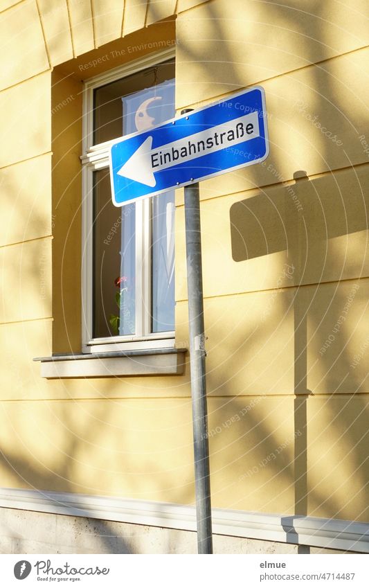 Traffic sign - one-way street pointing left - and its shadow on a residential house with window and moon behind the glass pane / VZ 220-10 One-way street