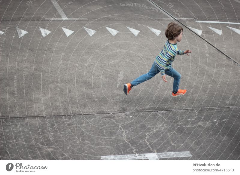 Child running across a square with arrows Running Speed swift Arrow Dynamics Walking Movement move Infancy Athletic Sports Playing urban Town Parking lot Empty