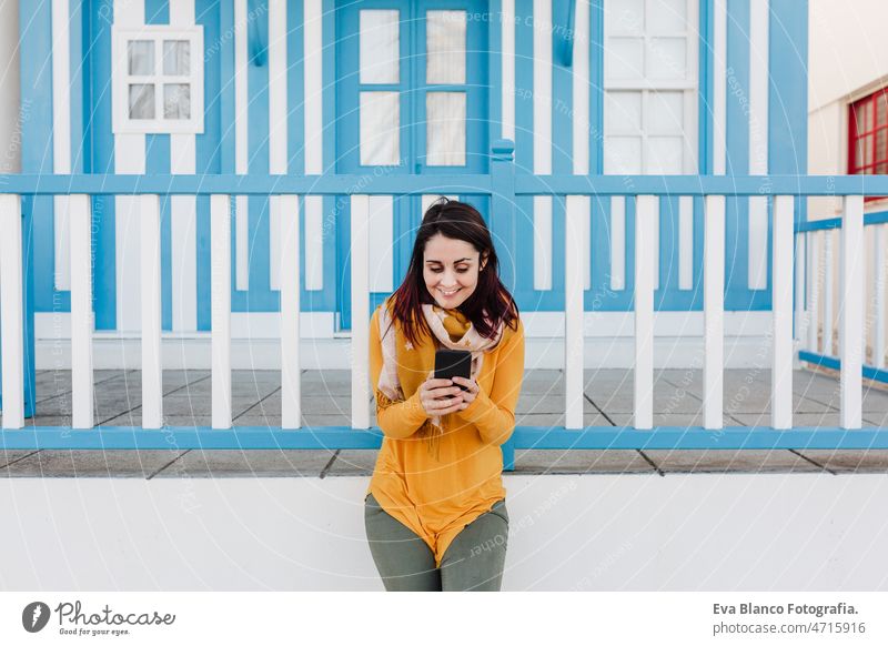 happy woman using mobile phone in front of colorful houses.Costa Nova, Aveiro, Portugal travel tourist enjoy aveiro portugal costa nova tourism backpacker