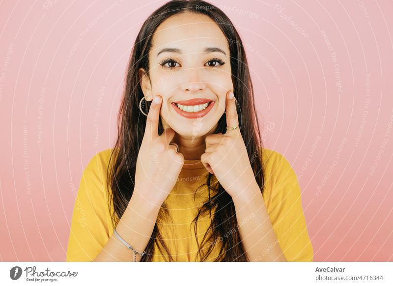 Young african woman close up portrait fingers on cheeks pointing smile gesture, cute and modern posing isolated over yellow color wall background. Daily expressions with copy space in studio.