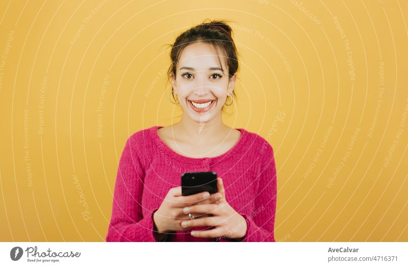 Young african woman checking happy his smart phone receiving good news posing isolated over yellow color wall background. Daily expressions with copy space in studio.