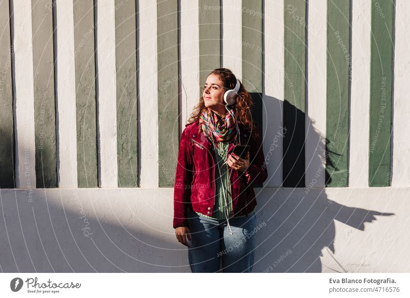 relaxed woman listening to music on headset.colorful houses.promenade Costa Nova, Aveiro, Portugal city sunny 30s caucasian happy headphones mobile phone