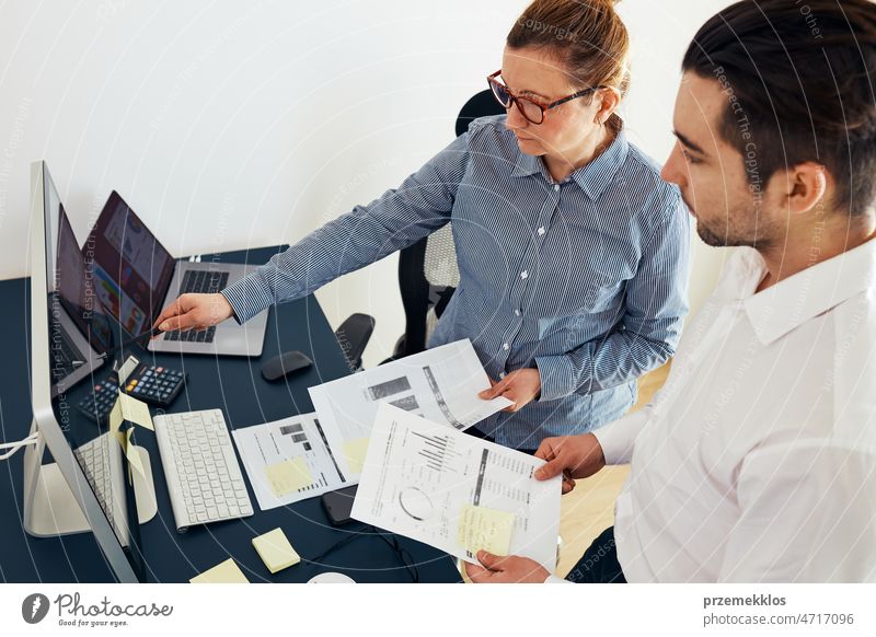 Businesswoman discussing financial data with her colleague standing at desk in office. Woman entrepreneur working with charts and tables on computer. Two people working together