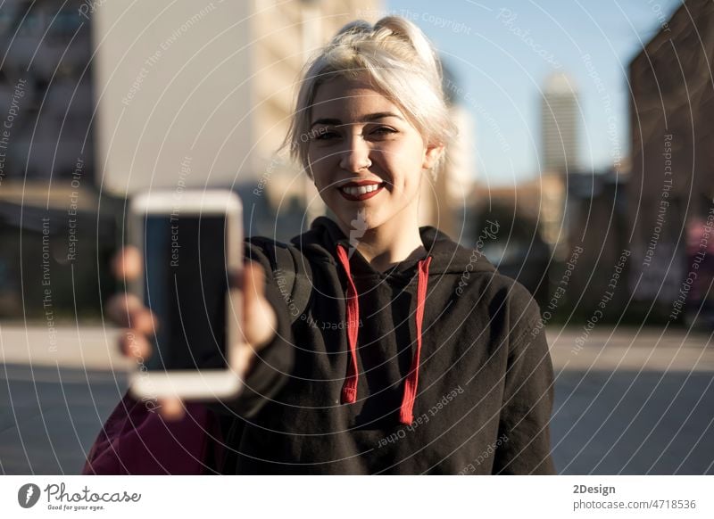 Woman standing against the city holding out a blank mobile phone towards the camera with focus to the person 20s cell display enjoy listen message mobility