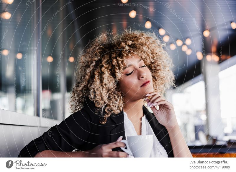 relaxed hispanic business woman in cafe with eyes closed. tech and lifestyle laptop computer afro working networking drinking coffee terrace outdoors goggles