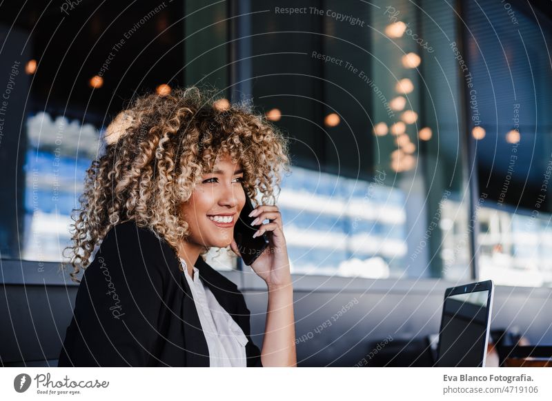 smiling hispanic business woman in cafe working on laptop and mobile phone. tech and lifestyle computer afro networking drinking coffee terrace outdoors goggles